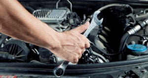 A man holding a silver wrench preparing to work under the hood of a car.