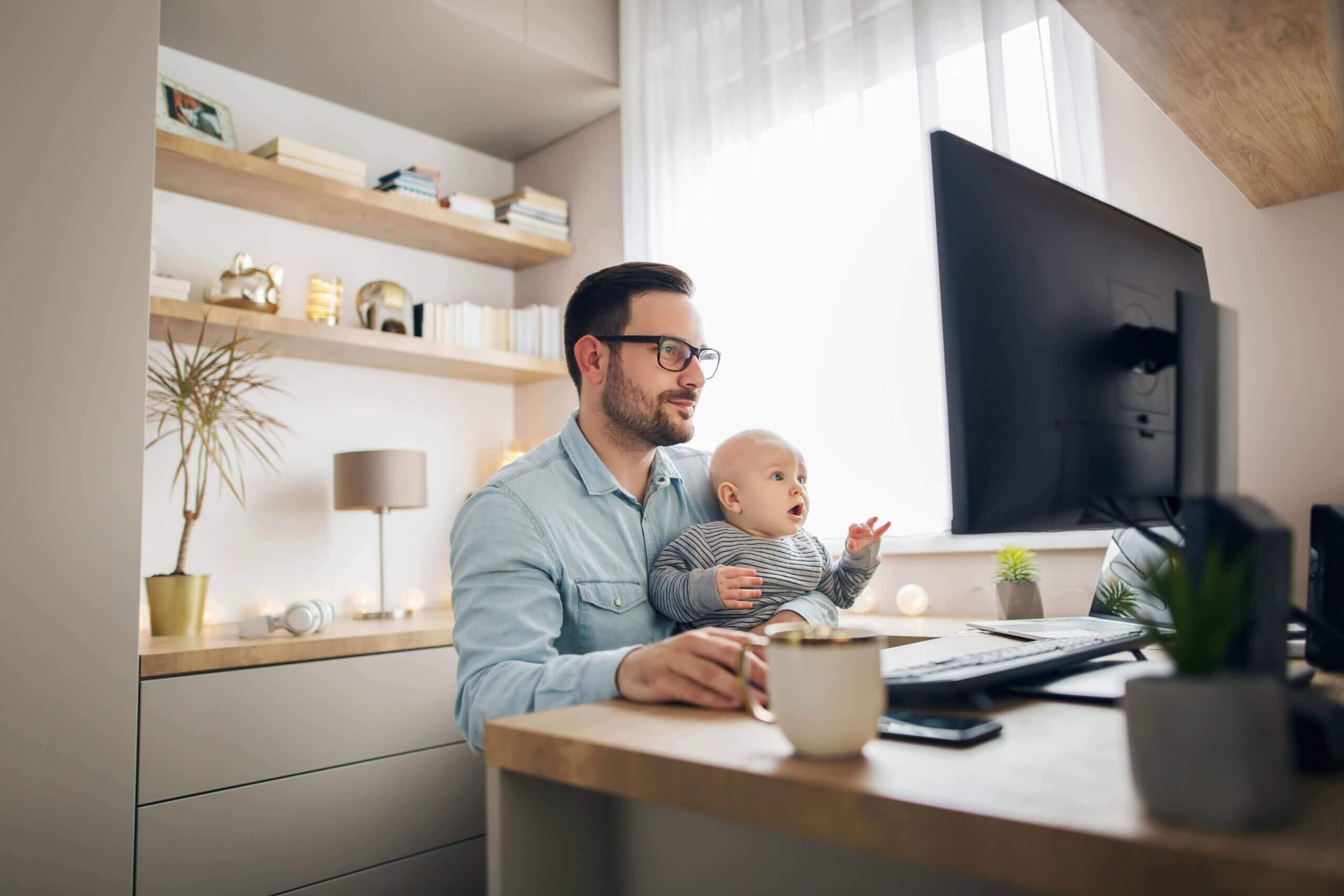 A Man holding baby and working at home.