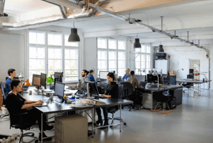 Open concept office, many workers at computers, desks.