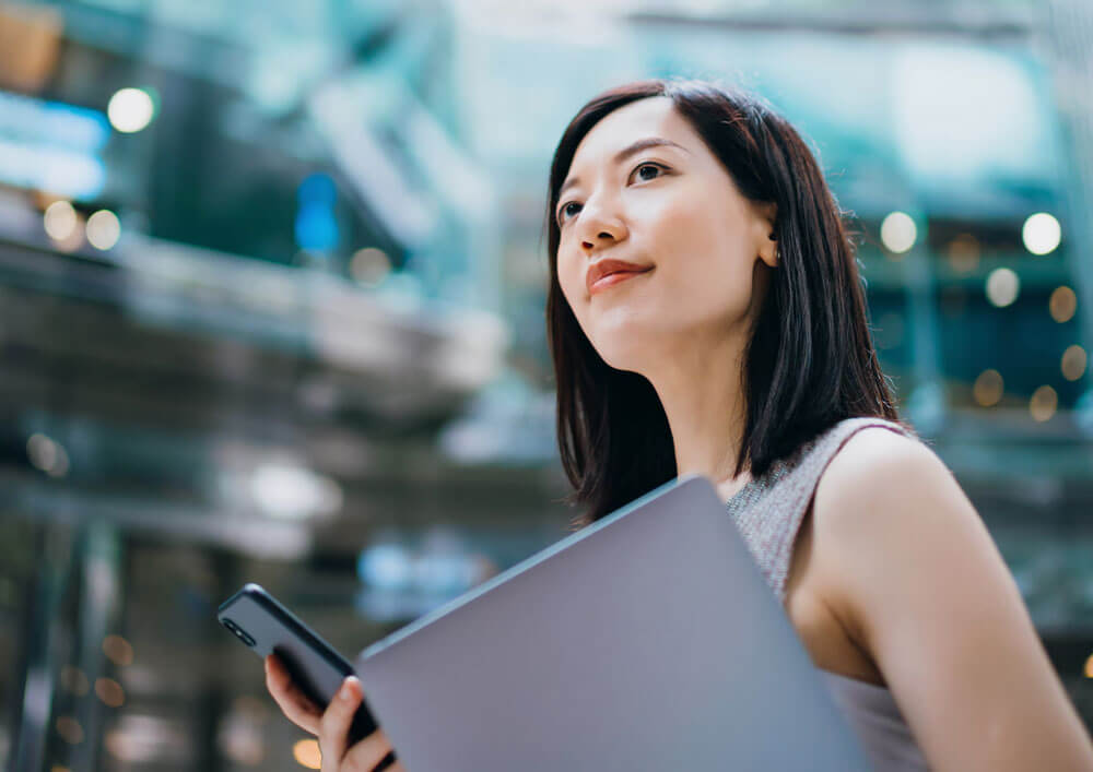 A Women Holding Laptop and Mobile is looking at sky