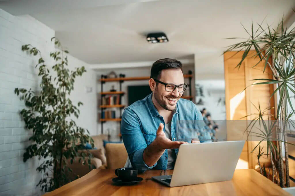 A man is on a video call on wood desk and plants