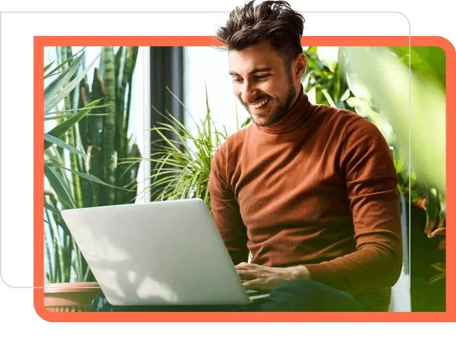man in orange sweater at laptop with plants