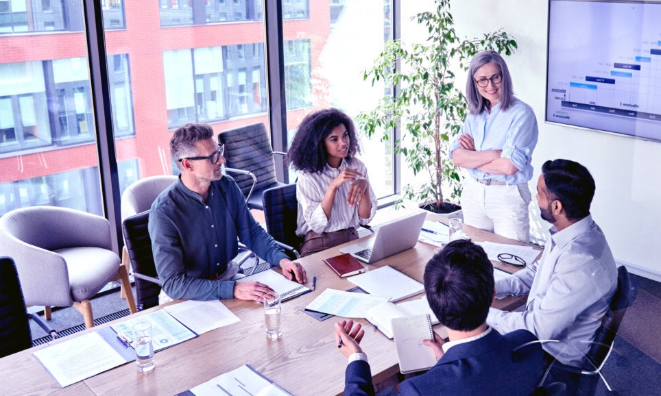Senior female ceo and multicultural business people discussing company presentation at boardroom table.